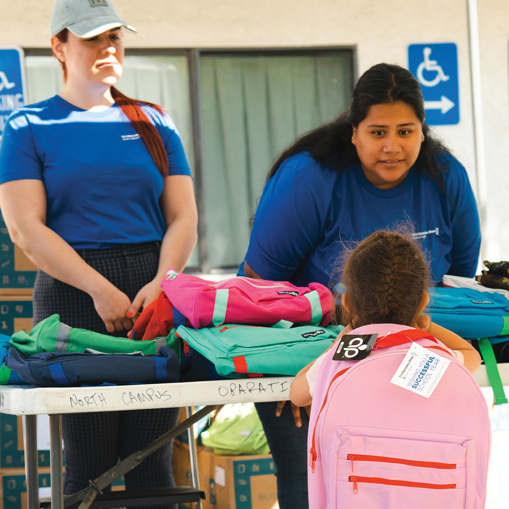 two colleagues give backpack to student