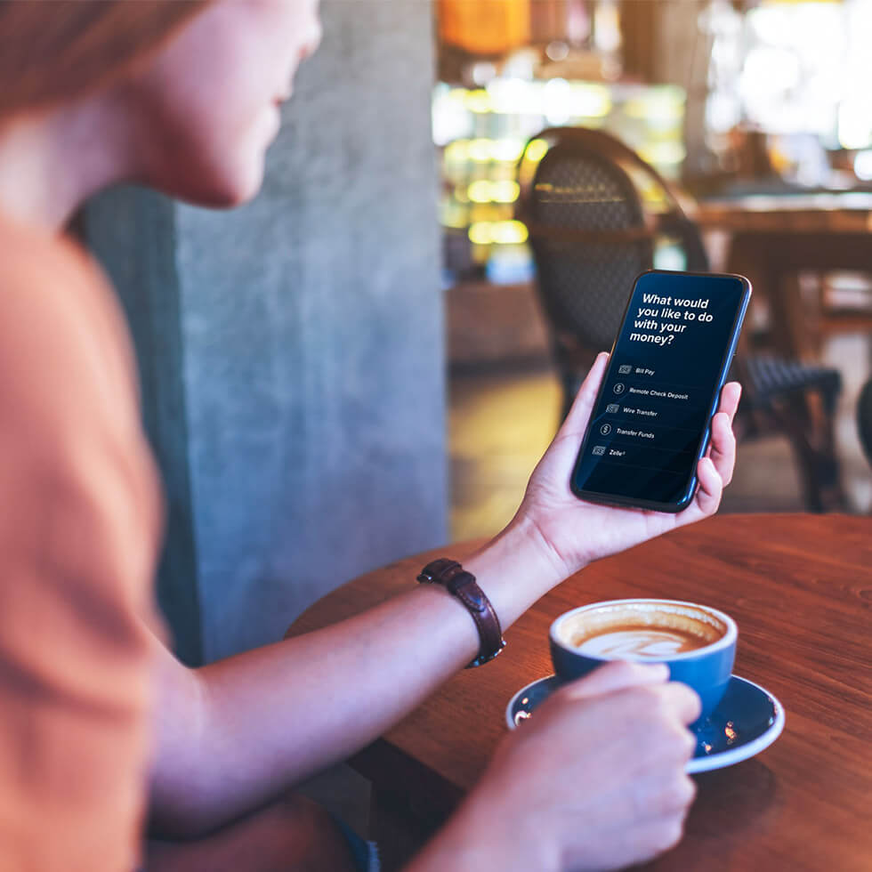 Woman at the coffee shop holding her iPhone and banking with City National Bank App