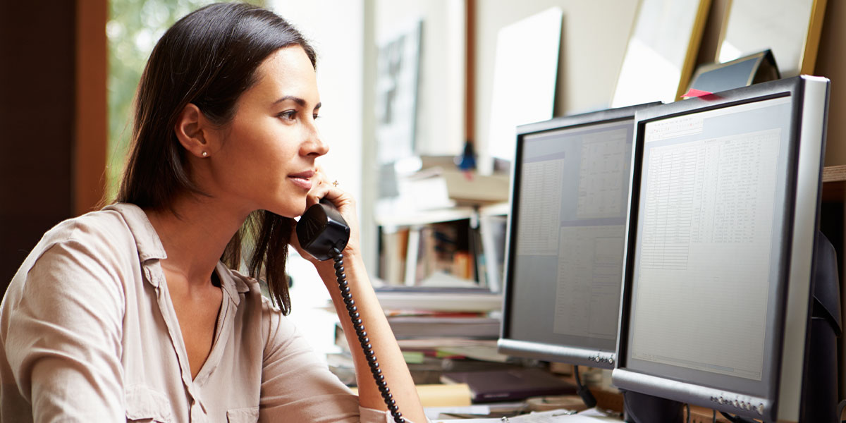 Business women sitting at her computer on the phone while managing accounts payable tasks.