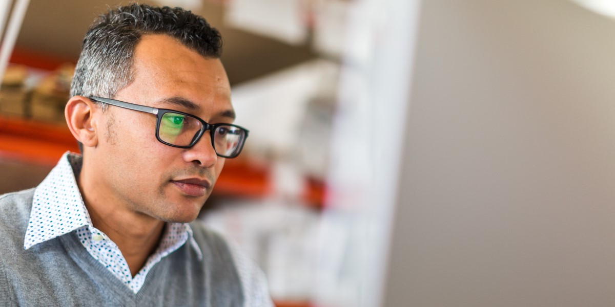  A man with glasses looks at his laptop screen