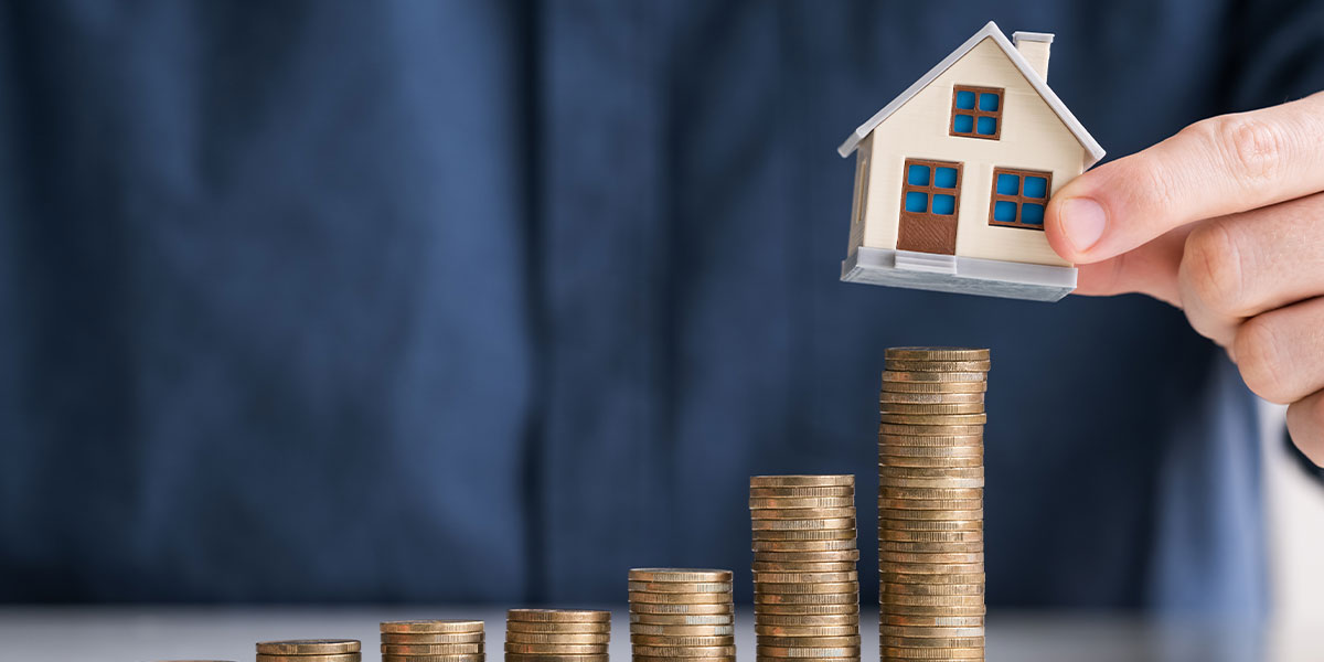 Person stacking model house on pile of coins