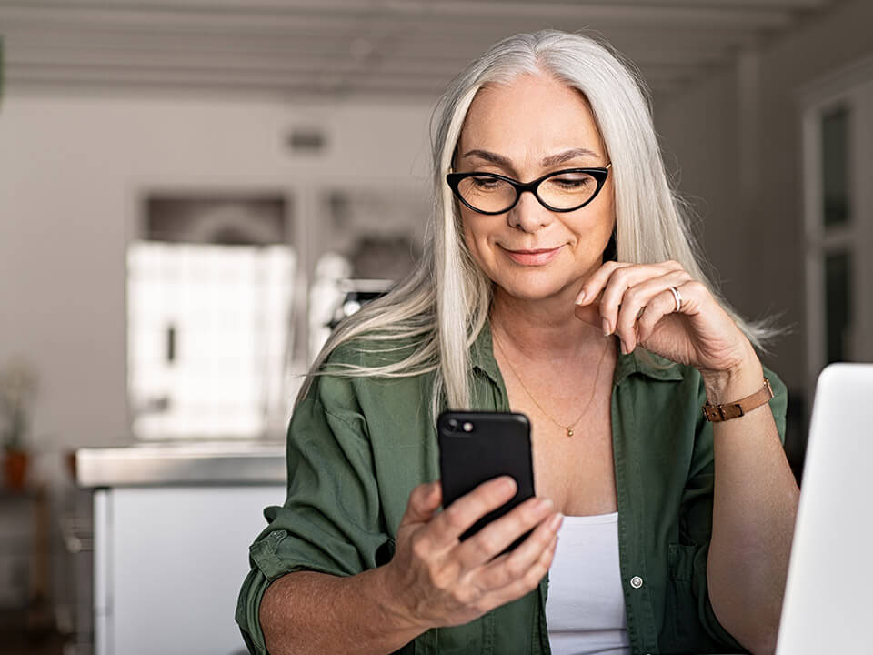 Senior woman in glasses logs into her City National Bank Checking Account on her mobile device