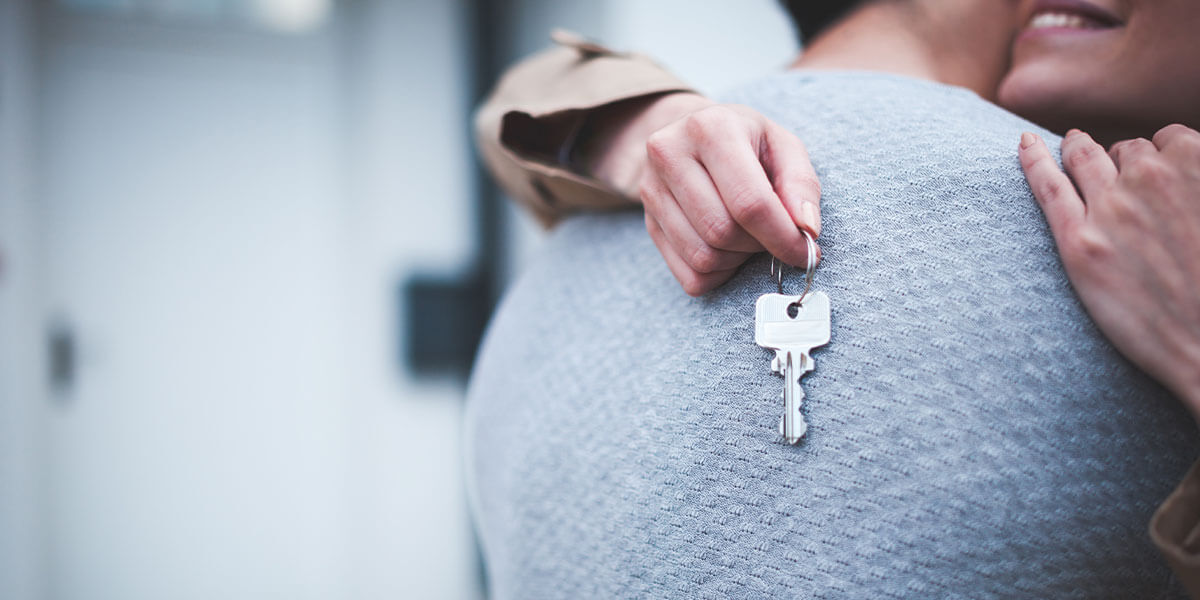 Couple embracing, holding keys after parents gifted a house to them. 