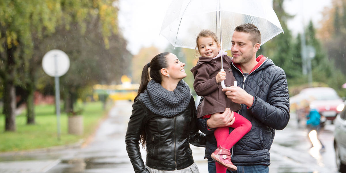 Couple with a daughter under an umbrella walking in the rain. 