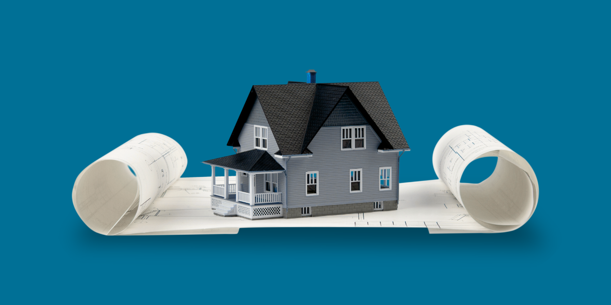 A miniature gray house with a pitched roof and front porch is placed on top of rolled-out architectural blueprints. The setting features a clean blue background, emphasizing the design and planning theme. The image conveys a sense of construction, architecture, and home design.