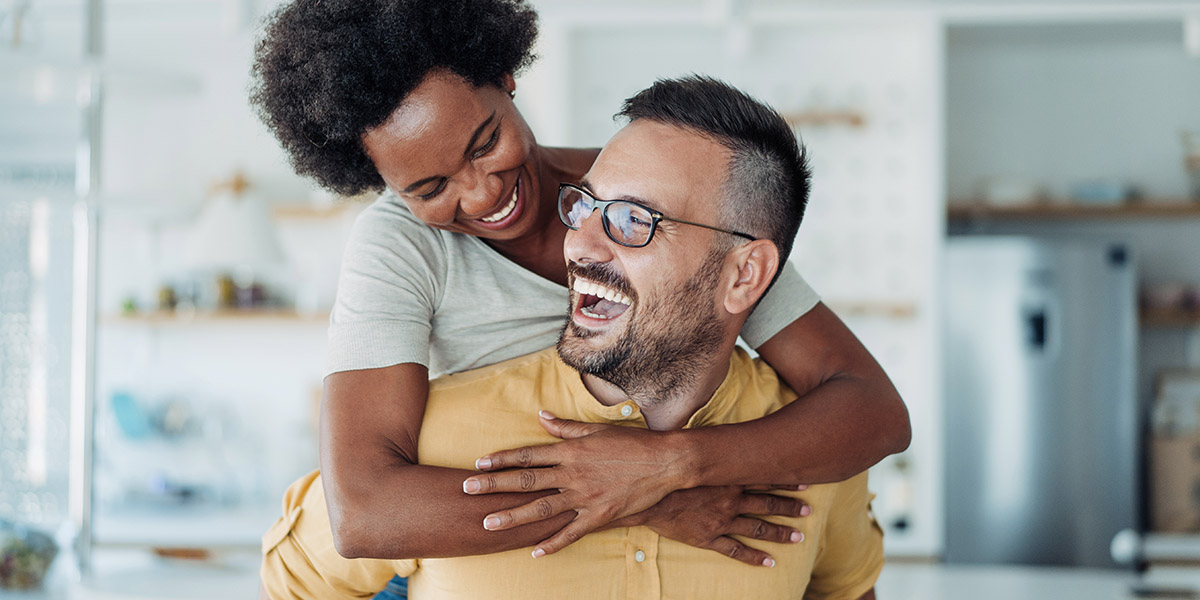 Shot of young couple spending leisure time together at home. Smiling girl piggybacking on her boyfriend. Playful man having fun while piggybacking his girlfriend. Happy man giving piggyback ride to woman in the living room.