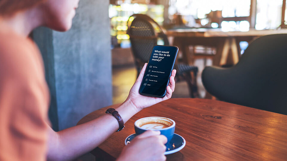 Woman at the coffee shop holding her iPhone and banking with City National Bank App