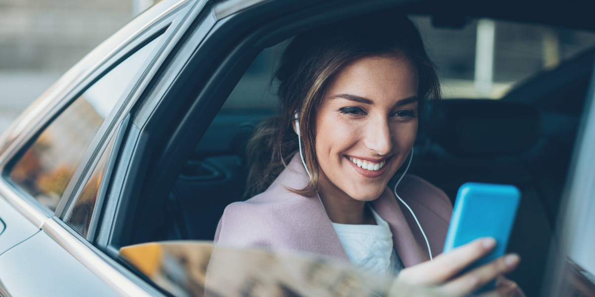 A woman looks at her phone while riding in the back of a car